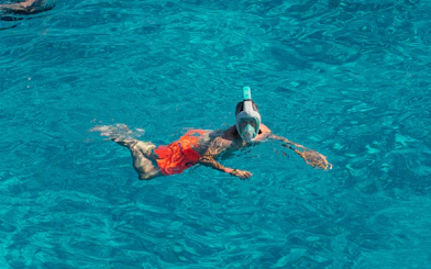 Snorkeler in clear blue water at Cala Bassa beach, Ibiza, Spain.