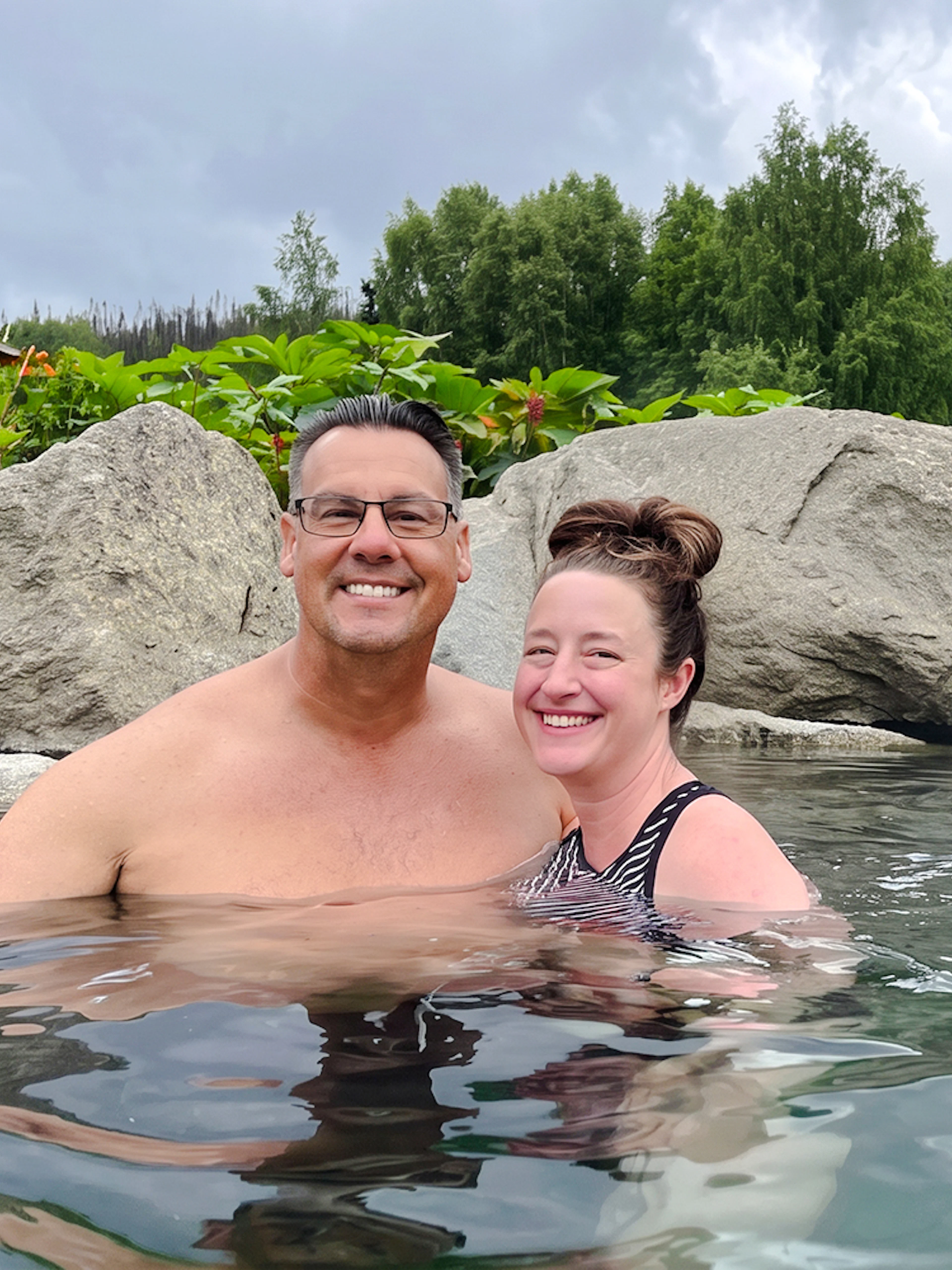 Couple enjoying Chena Hot Springs with rocky backdrop and lush greenery.