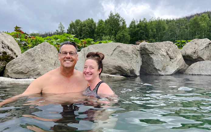 Couple enjoying Chena Hot Springs with rocky backdrop and lush greenery.