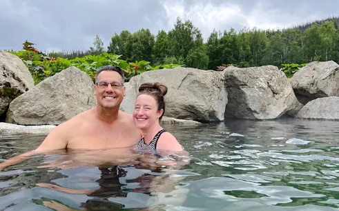 Couple enjoying Chena Hot Springs with rocky backdrop and lush greenery.