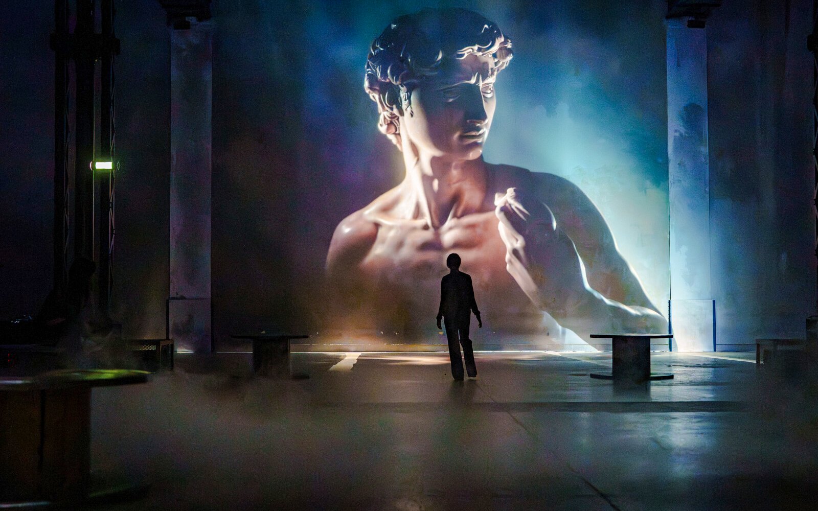 Visitor at Renaissance immersive experience, Atelier des Lumières, Paris, with David sculpture projection.