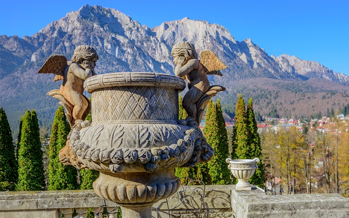 Sculpture of cherubs inside Cantacuzino Palace with mountain backdrop.