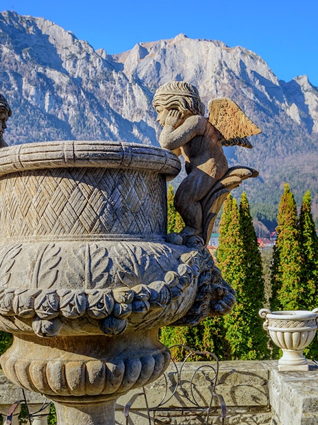Sculpture of cherubs inside Cantacuzino Palace with mountain backdrop.