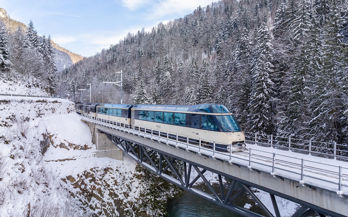 Interrail train crossing snowy bridge in winter forest.