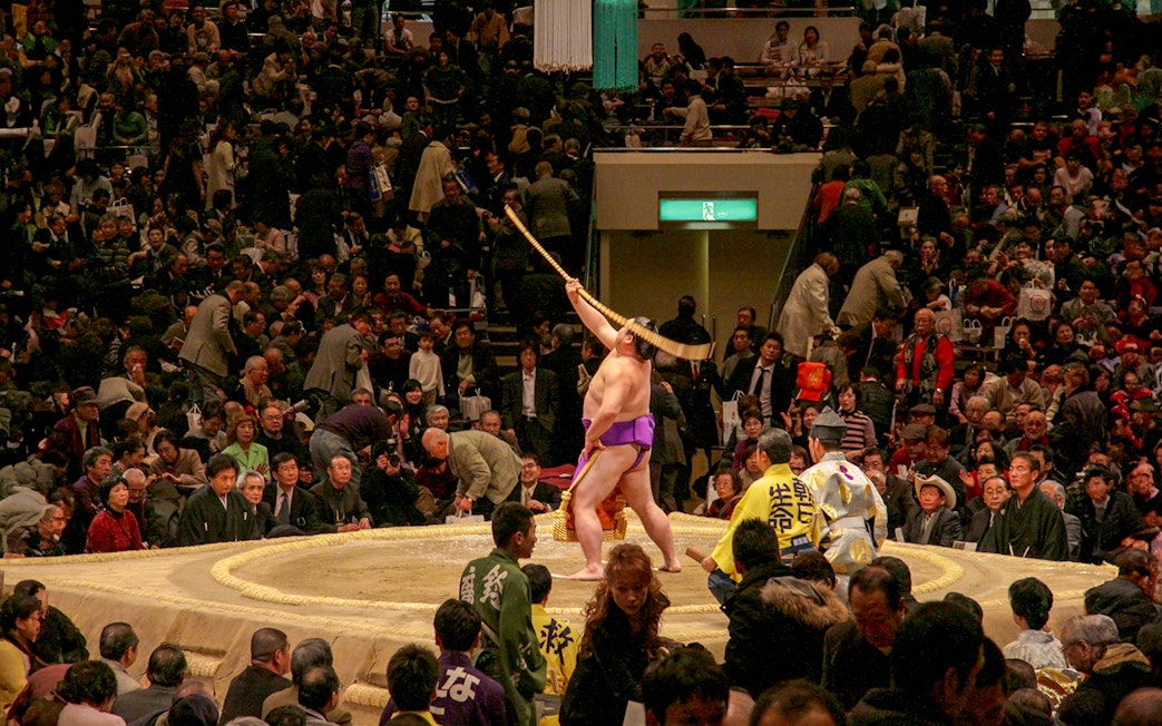 Sumo wrestler performing ritual at Fukuoka tournament with audience watching.