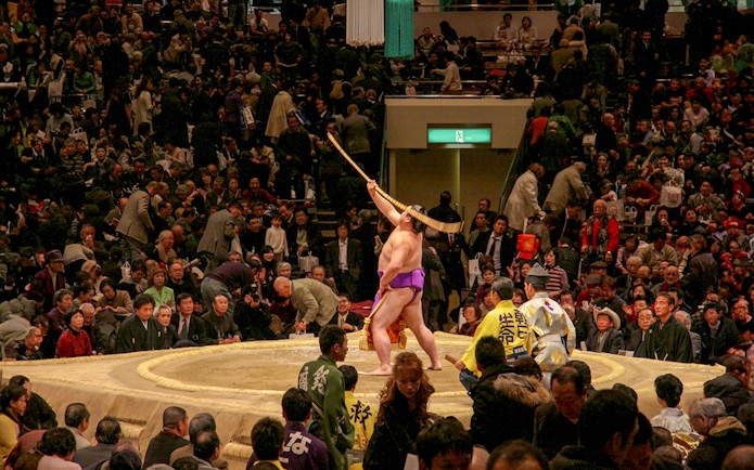 Sumo wrestler performing ritual at Fukuoka tournament with audience watching.