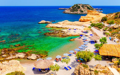 Beach with umbrellas and clear waters on Charaki Island, Rhodes, Greece.