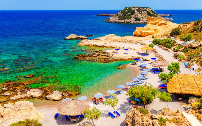 Beach with umbrellas and clear waters on Charaki Island, Rhodes, Greece.