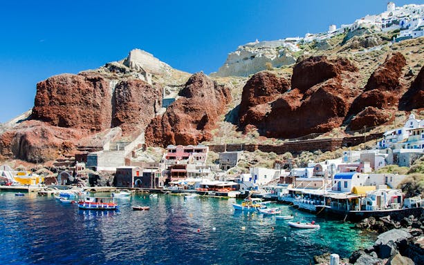 Boats docked at Amoudi Bay below the Oia caldera cliffs in Santorini, Greece.