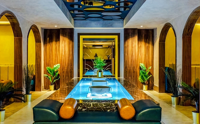 Private Turkish bath interior with central pool, wooden arches, and potted plants.