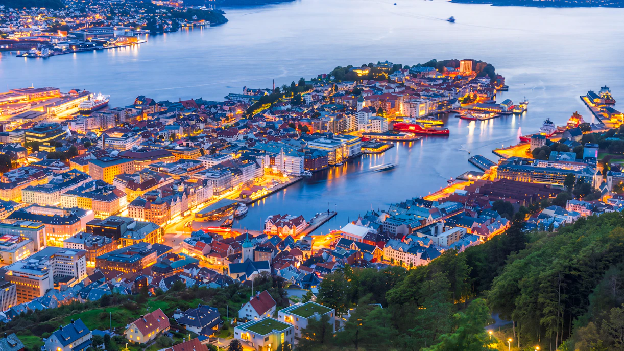 Night view of Bergen cityscape from Mount Fløyen, showcasing illuminated buildings and harbor.