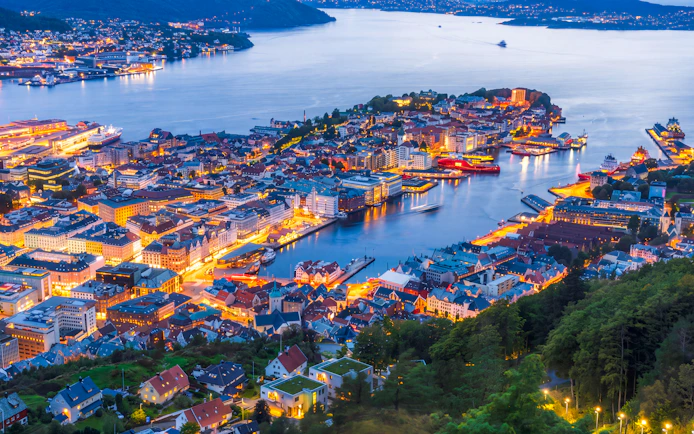 Night view of Bergen cityscape from Mount Fløyen, showcasing illuminated buildings and harbor.