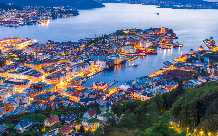 Night view of Bergen cityscape from Mount Fløyen, showcasing illuminated buildings and harbor.