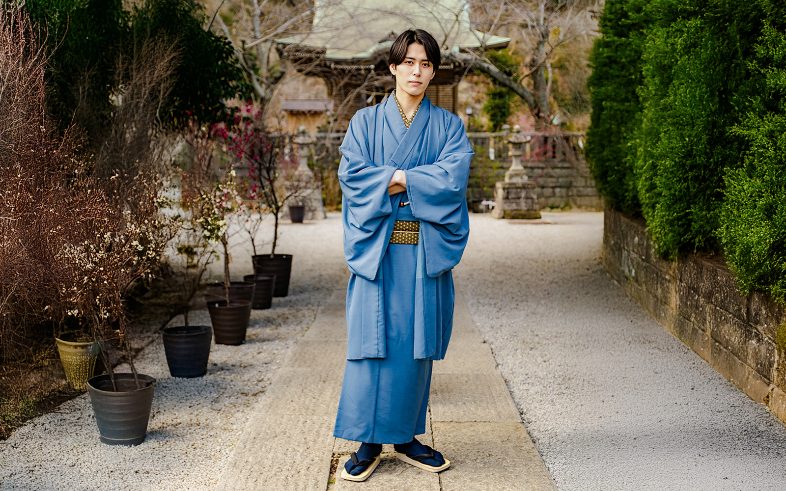Man in blue Yukata standing in a Japanese garden pathway.