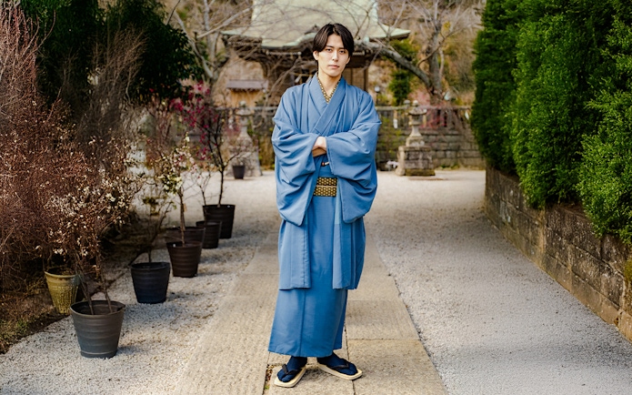 Man in blue Yukata standing in a Japanese garden pathway.