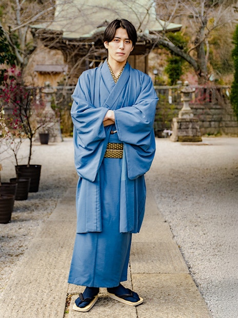Man in blue Yukata standing in a Japanese garden pathway.