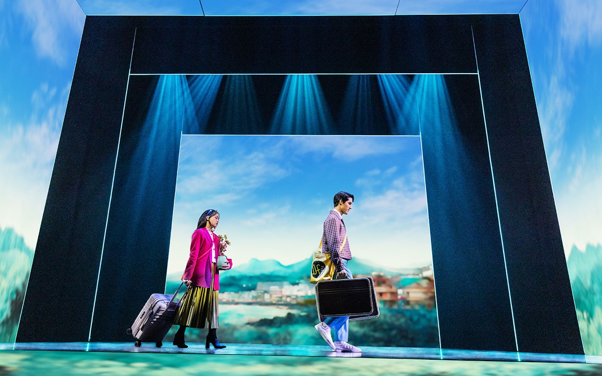 Actors on stage during Maybe Happy Ending Broadway show, carrying suitcases with scenic backdrop.