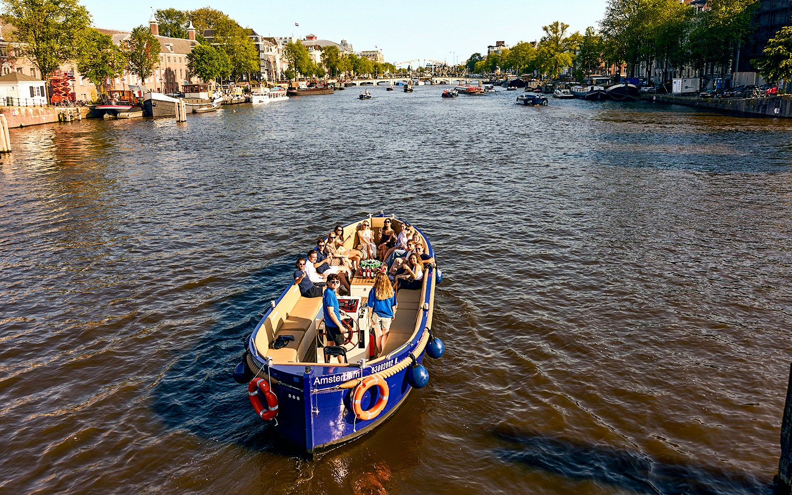 Amsterdam canal cruise boat with passengers enjoying drinks.