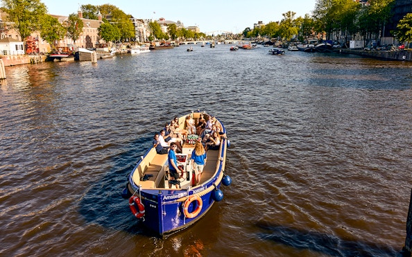 Amsterdam canal cruise boat with passengers enjoying drinks.