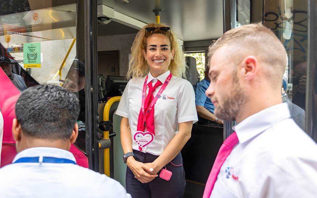 Open bus crew members welcoming passengers onboard.
