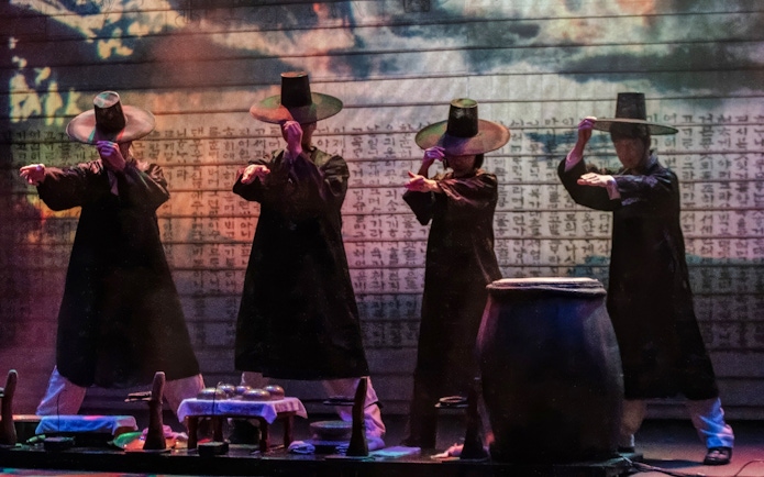 Performers in traditional attire at NANTA Musical Show, Myeongdong, with Korean script backdrop.