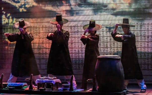 Performers in traditional attire at NANTA Musical Show, Myeongdong, with Korean script backdrop.