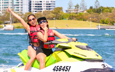 Jet ski riders enjoying a water adventure near cityscape backdrop.