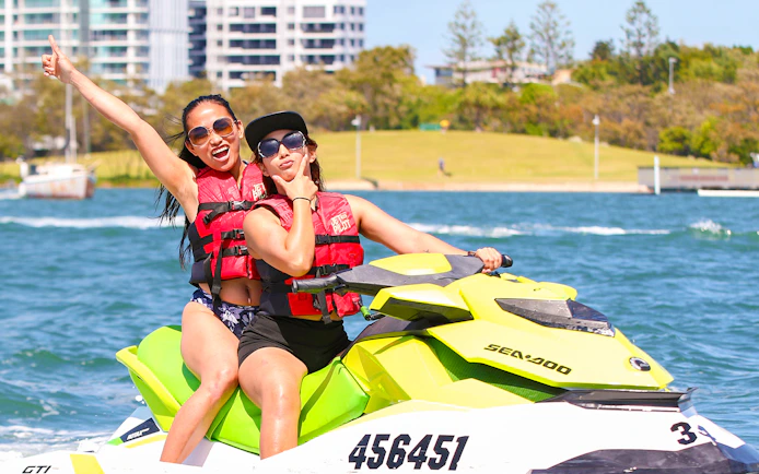 Jet ski riders enjoying a water adventure near cityscape backdrop.