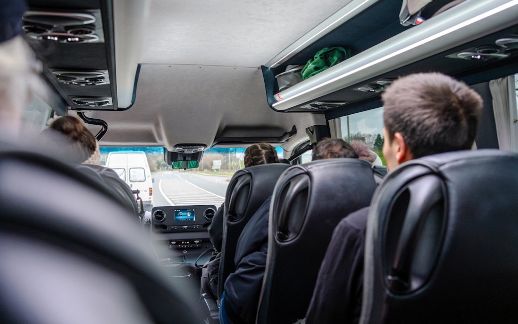 Inside view of a guided bus tour with passengers seated, traveling on a highway.