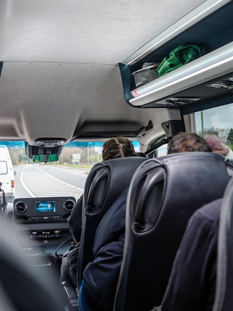 Inside view of a guided bus tour with passengers seated, traveling on a highway.