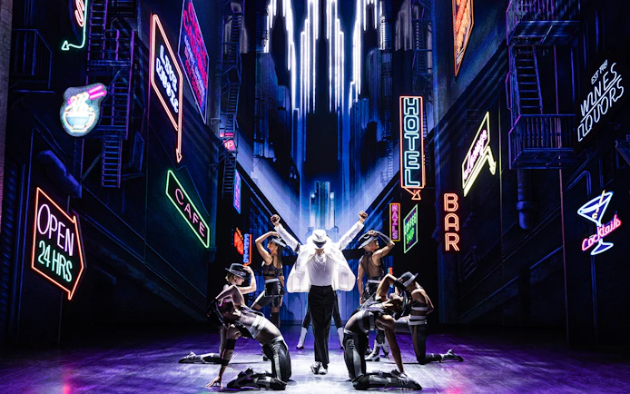 Performer in white suit and dancers on stage with neon cityscape backdrop at MJ Live Tribute Concert.