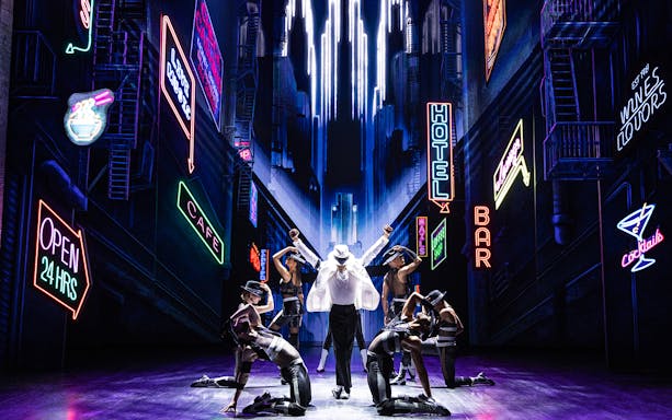 Performer in white suit and dancers on stage with neon cityscape backdrop at MJ Live Tribute Concert.