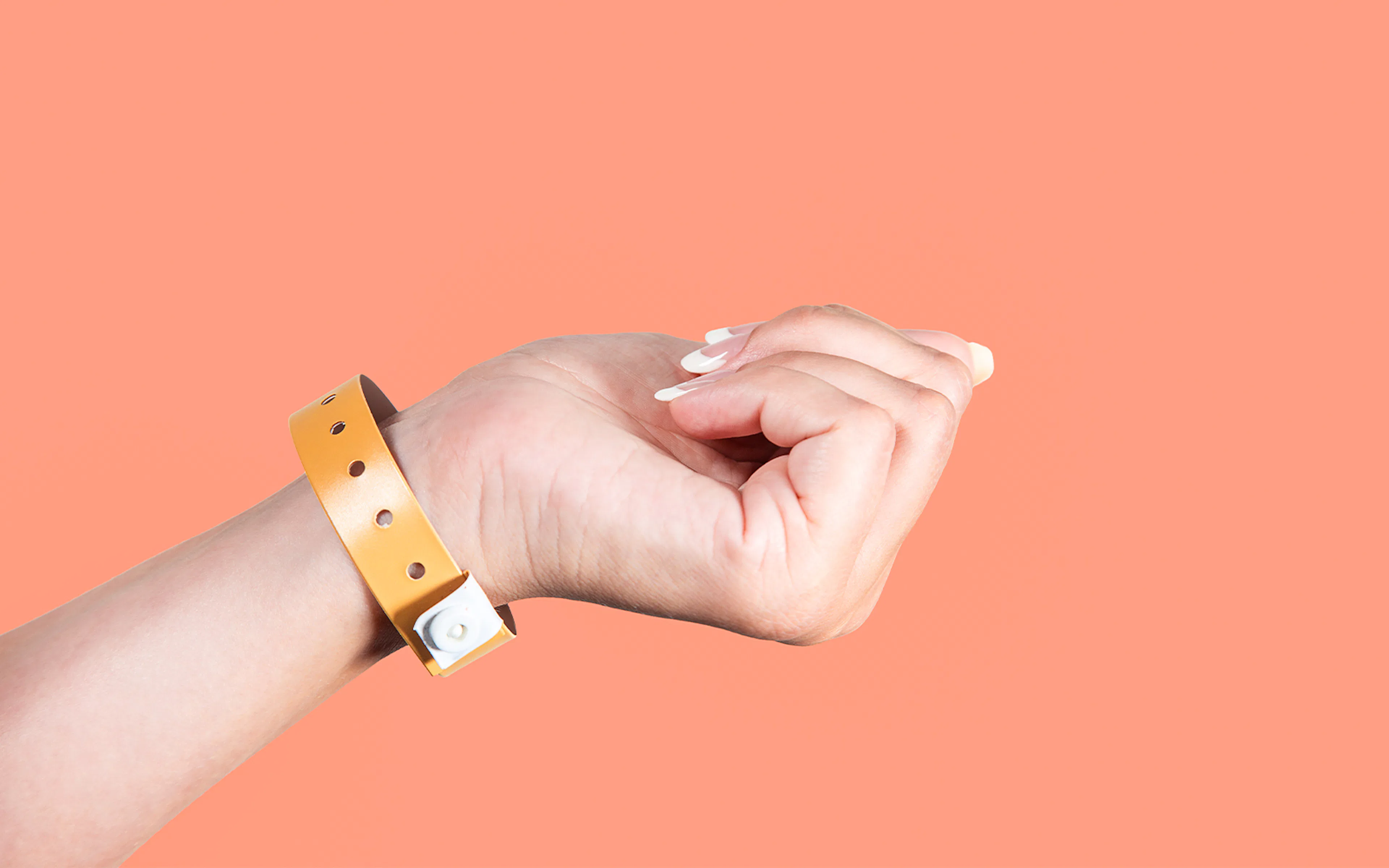 Hand wearing brown entrance wristband against peach background.