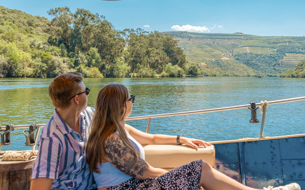 Tourists enjoying a boat ride on the Douro River with scenic vineyard views.