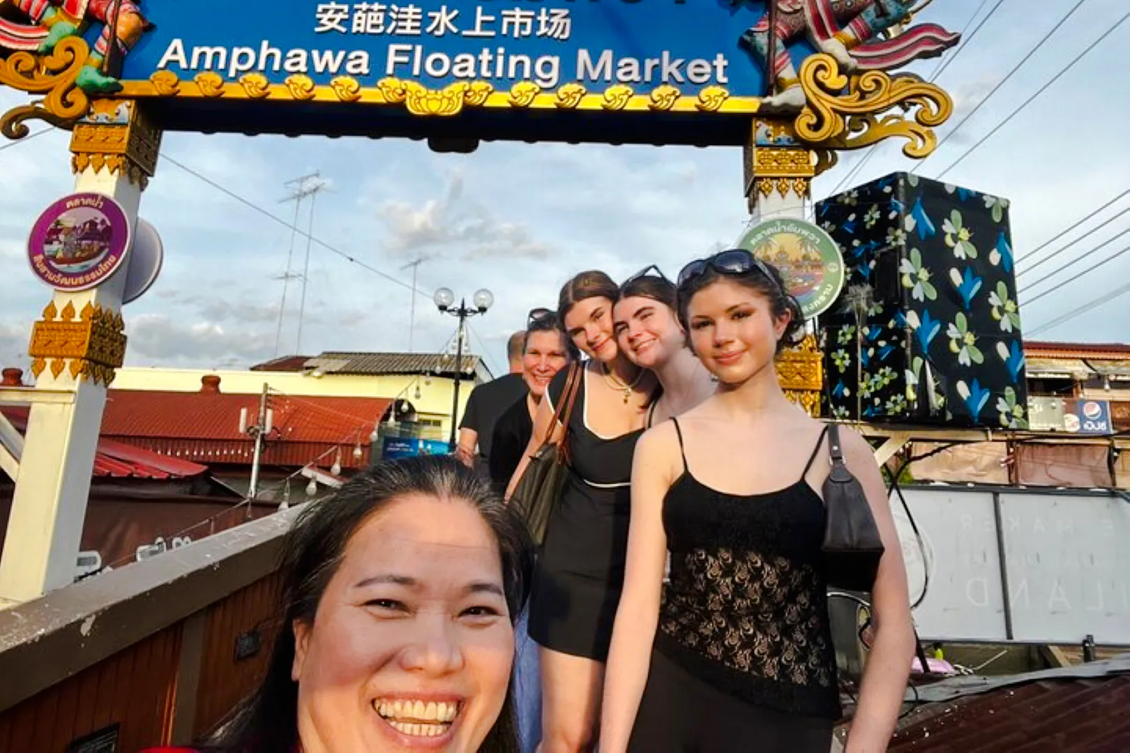 Visitors smiling under the Amphawa Floating Market sign during a private shore excursion from Laem Chabang, Pattaya.