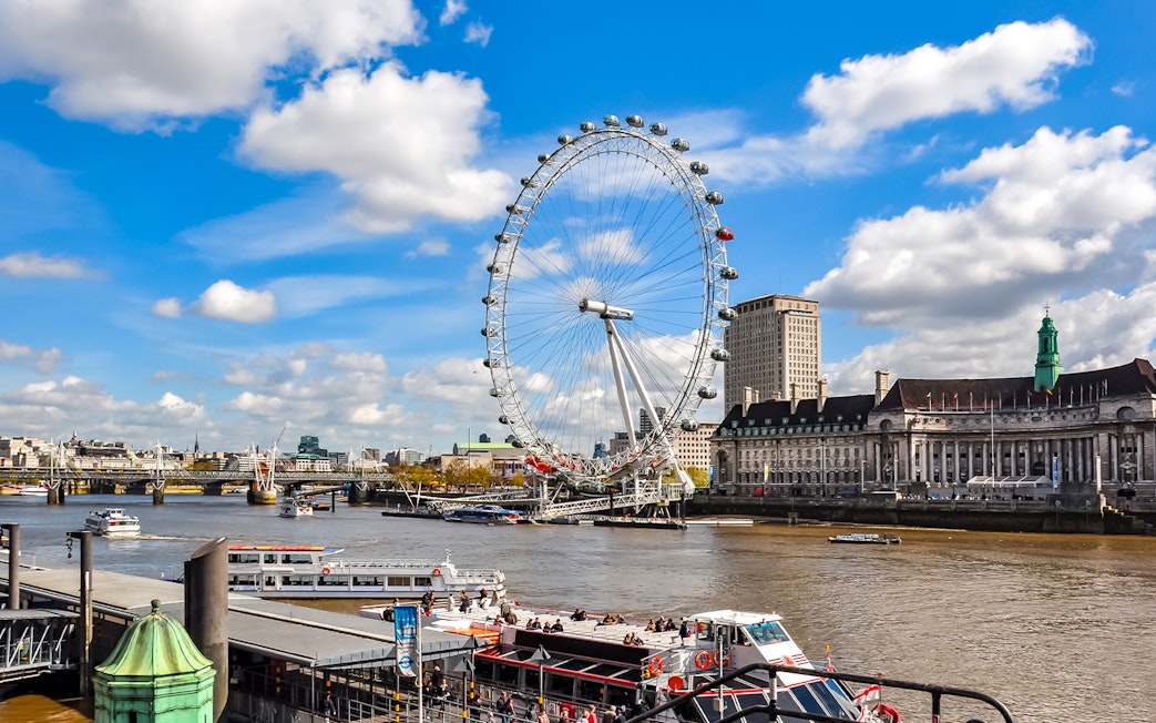 London Eye on the Thames River with nearby historic buildings, UK.