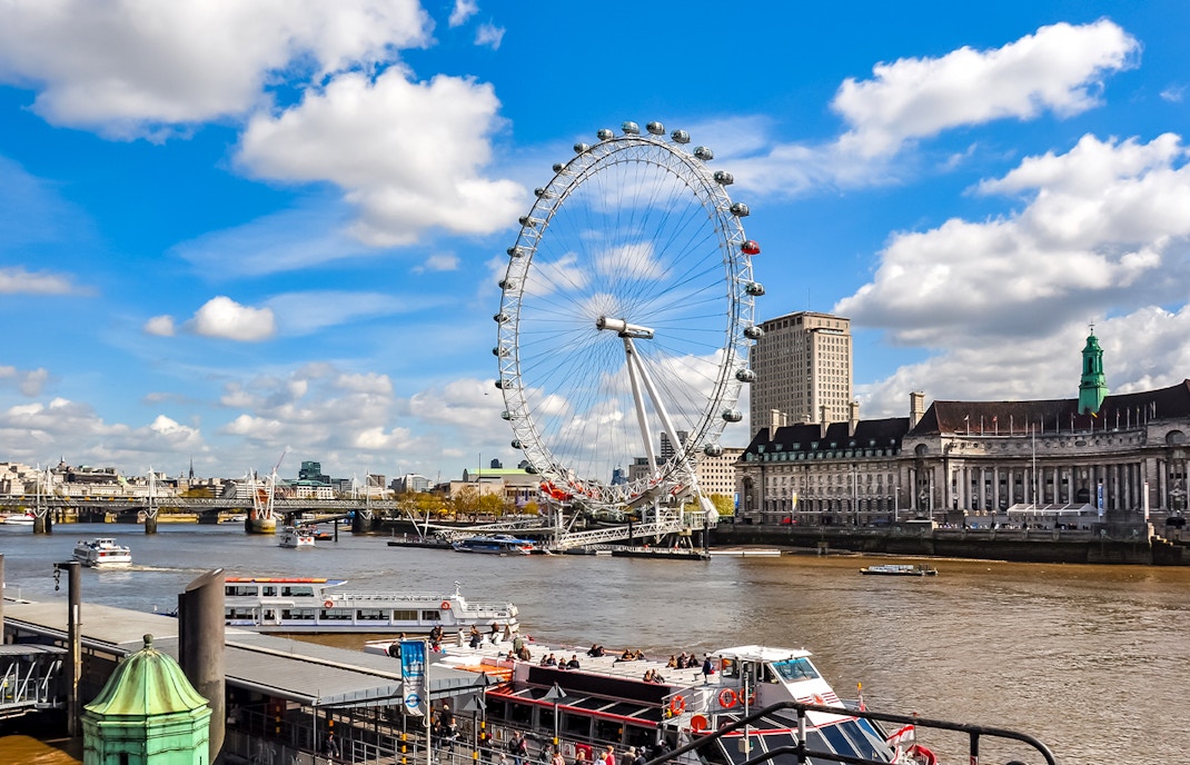 London Eye on the Thames River with nearby historic buildings, UK.