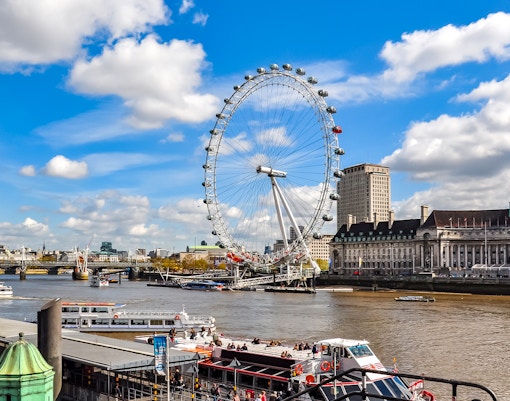 London Eye on the Thames River with nearby historic buildings, UK.