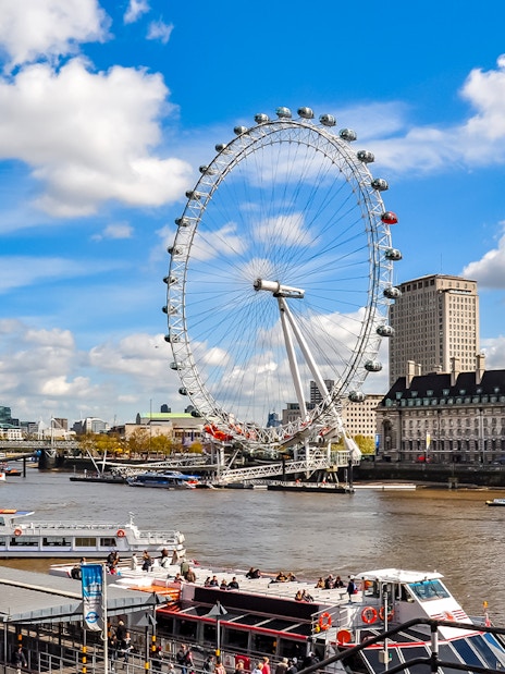 London Eye on the Thames River with nearby historic buildings, UK.