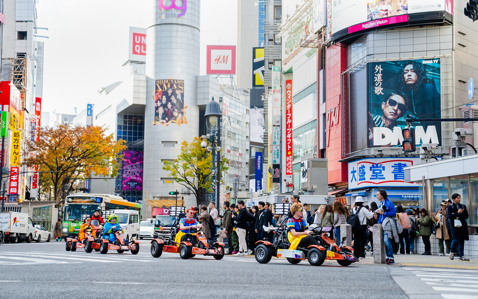 Tourists go-karting in Shibuya, Tokyo, surrounded by city buildings and billboards.