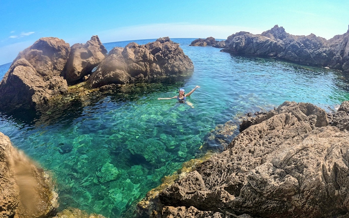 Swimmer enjoying clear waters near rocky cliffs on Dubrovnik boat tour.