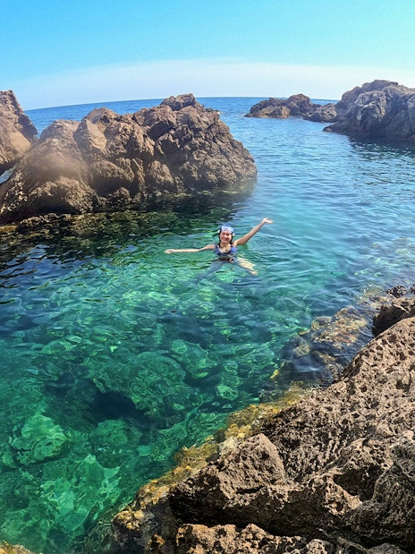 Swimmer enjoying clear waters near rocky cliffs on Dubrovnik boat tour.