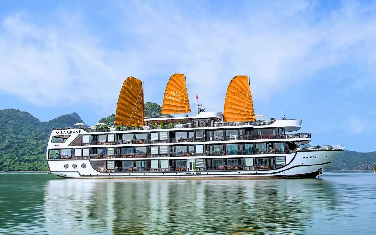 Luxury cruise ship with orange sails on Lan Ha Bay, Vietnam, surrounded by green hills.
