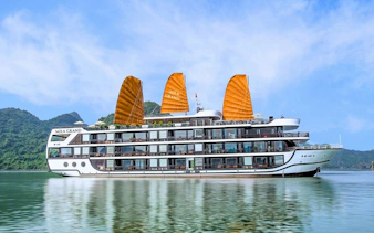 Luxury cruise ship with orange sails on Lan Ha Bay, Vietnam, surrounded by green hills.
