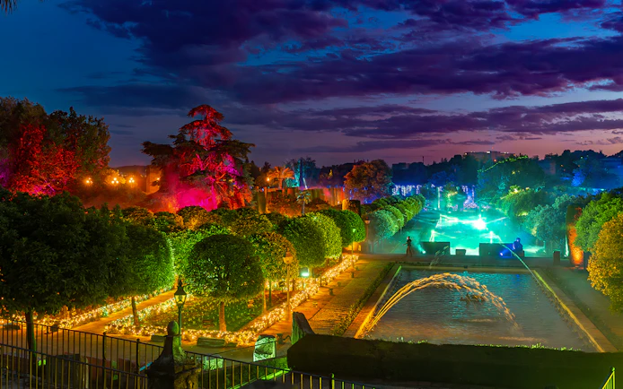 Alcazar of Cordoba garden illuminated at night with colorful lights and fountains.
