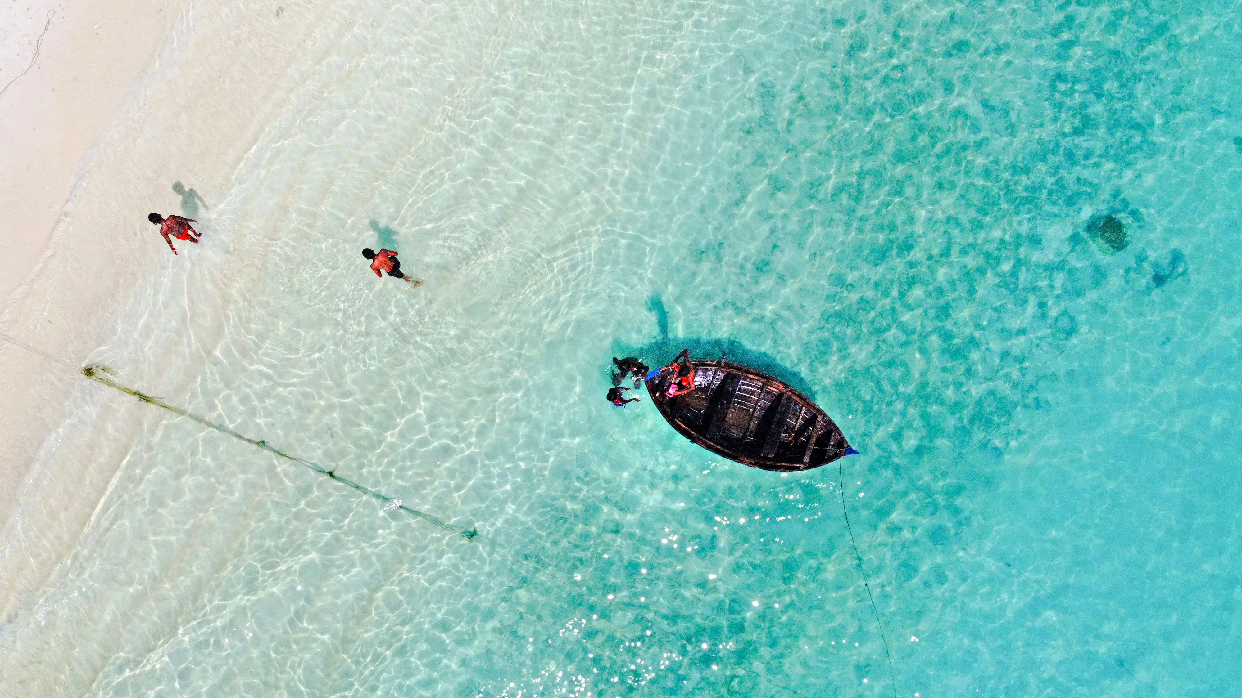 Snorkelers near a wooden boat in clear waters of Mnemba Island Atoll, Zanzibar.