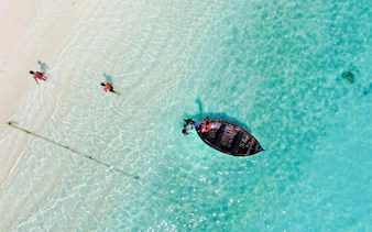 Snorkelers near a wooden boat in clear waters of Mnemba Island Atoll, Zanzibar.