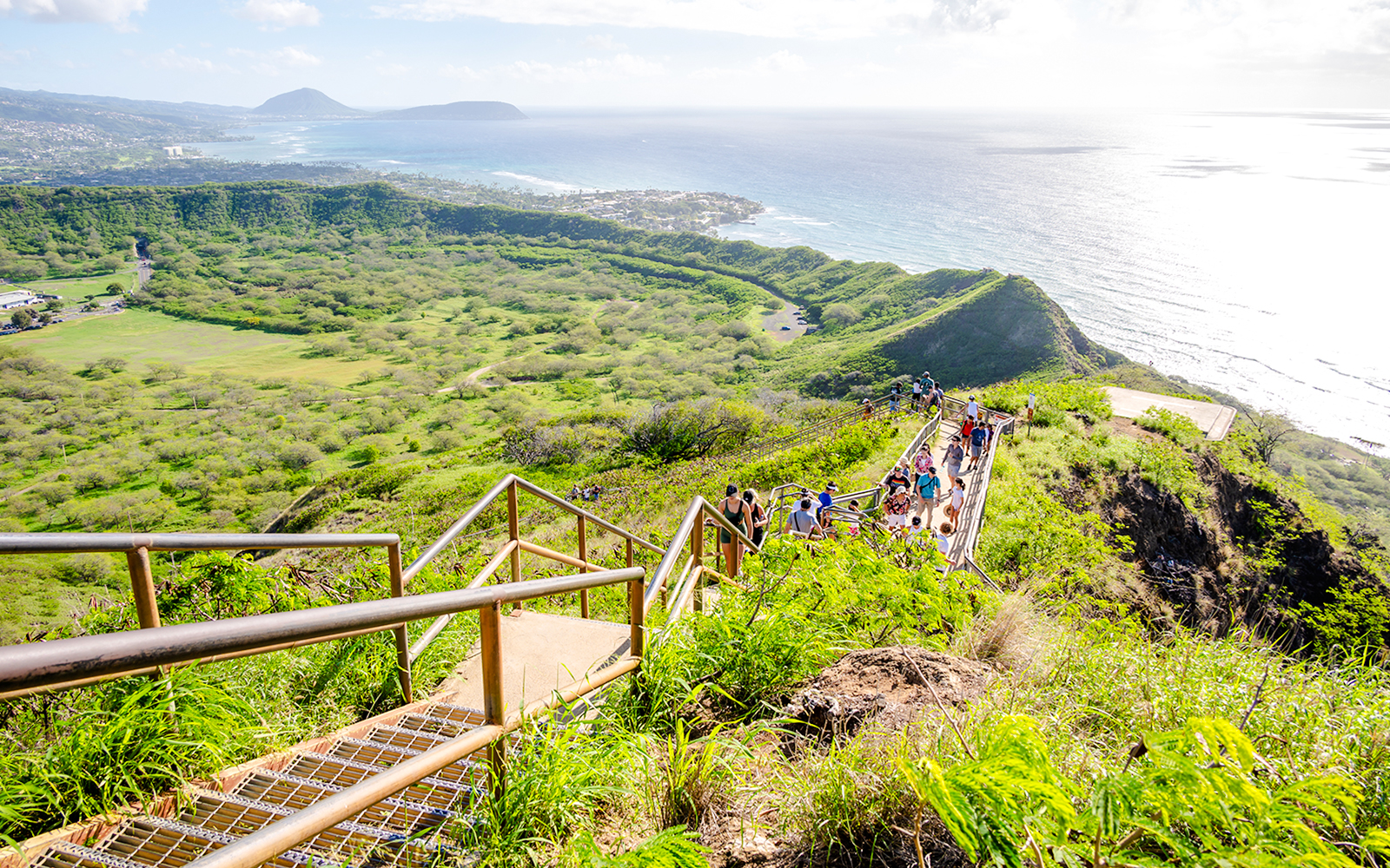 Tourists hiking on Diamond Head trail with ocean and landscape views.