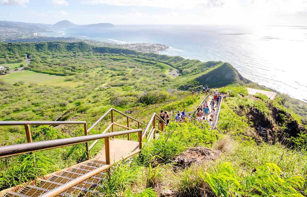 Tourists hiking on Diamond Head trail with ocean and landscape views.