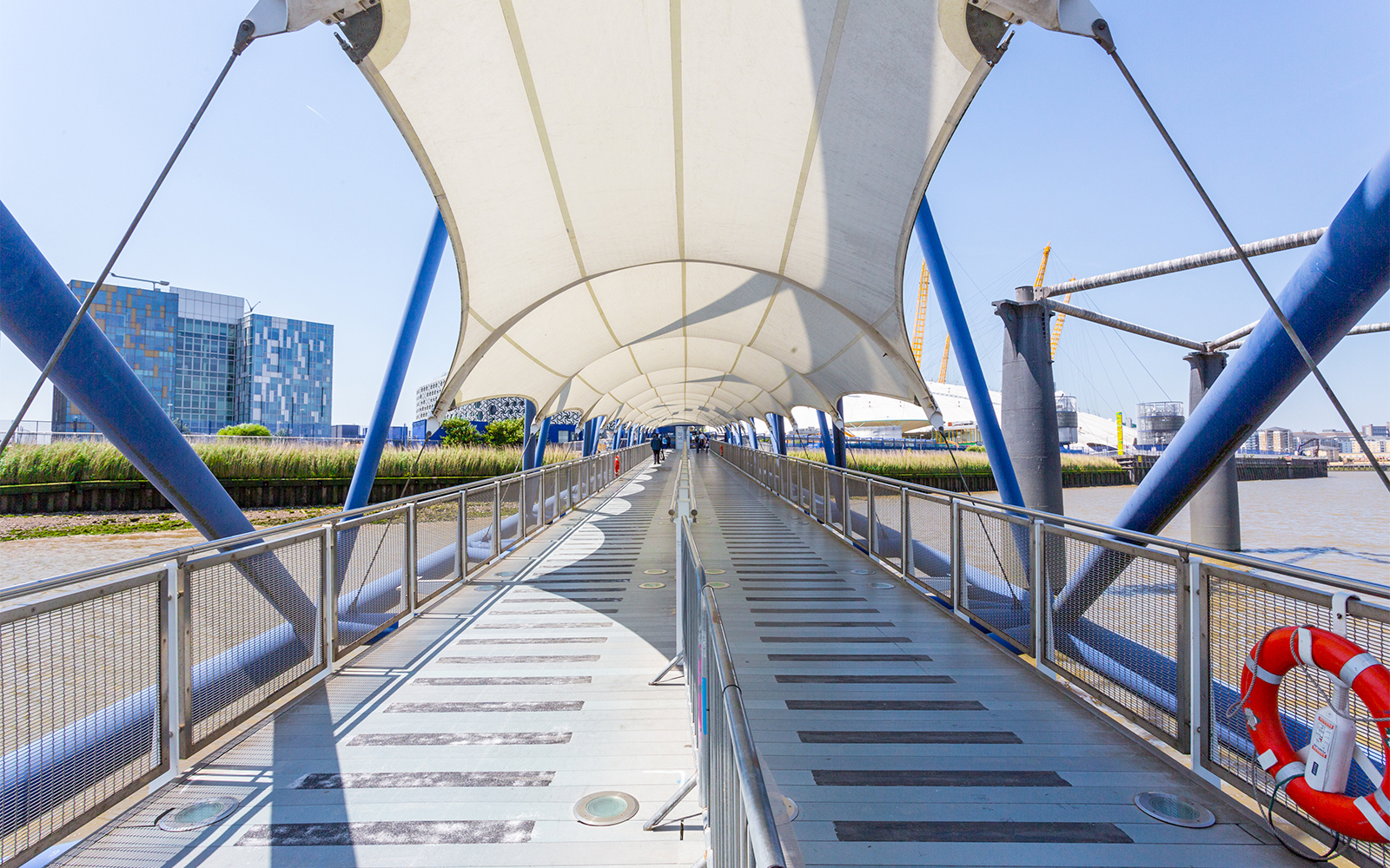 Covered walkway at Greenwich Pier with view of the Thames and modern buildings.